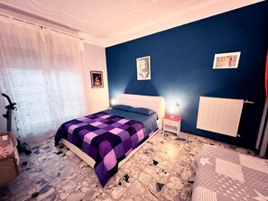 A bedroom with a bed, a nightstand, a radiator, and a window with curtains.