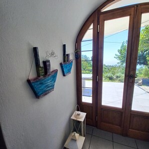 A room with a wooden door leading outside, a white wall, and a small table with a white lamp. - Country House 'The Arch House' with Sea View (Κύμη)