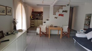 A living room with a sofa, a dining table with chairs, a kitchen area in the background, and a staircase leading to another level. - Country House 'The Arch House' with Sea View (Κύμη)