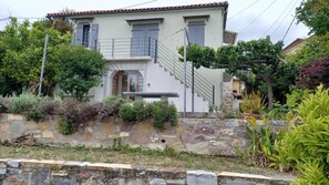 A two-story house with a stone retaining wall, a staircase, and a garden with various plants. - Country House 'The Arch House' with Sea View (Κύμη)