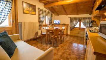 Una stanza accogliente con soffitto in legno, un tavolo da pranzo con sedie, un divano, una televisione e un angolo cottura con finestra.