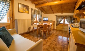 Una stanza accogliente con soffitto in legno, un tavolo da pranzo con sedie, un divano, una televisione e un angolo cottura con finestra.