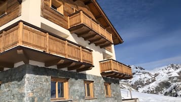 Un edificio in legno a più piani con balconi, una base in pietra e montagne innevate sullo sfondo.