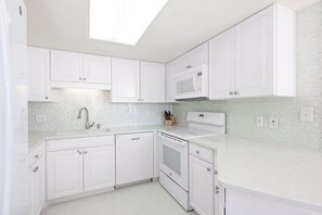 Een moderne keuken met witte kastjes, een roestvrijstalen spoelbak, een magnetron en een vaatwasser.