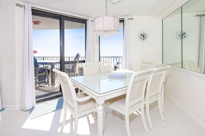 Een eetgedeelte met een glazen tafel en witte stoelen, een kroonluchter, en een balkon met uitzicht.