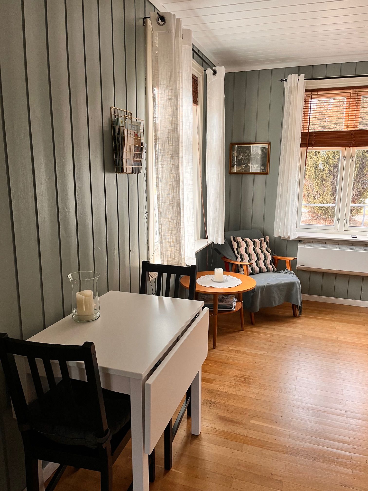 Une pièce comprenant une table à manger, des chaises, un canapé et une fenêtre avec des stores.