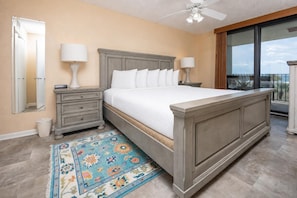 A bedroom with a bed, nightstands, a ceiling fan, a large window, and a view of the outdoors. - Phoenix Vi 6212 2 Bedroom Condo (Orange Beach)