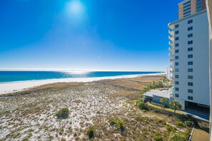 Une propriété située en bord de mer, offrant une vue dégagée sur l’océan, une plage de sable et un bâtiment moderne à plusieurs étages.