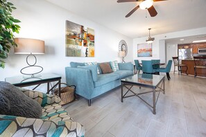 A modern living room with a sofa, coffee table, and chairs, a dining area with a table and chairs, and a kitchen with appliances. - Phoenix Vi 6714 2 Bedroom Condo (Orange Beach)