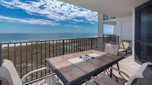 Een balkon met een tafel en stoelen, met uitzicht op een strand en een heldere lucht.