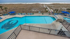A swimming pool with a shark design, surrounded by lounge chairs and umbrellas, overlooking a beach. - Phoenix Vi 6309 2 Bedroom Condo (Orange Beach)