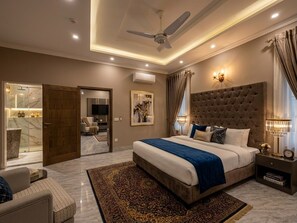 Ein modernes Schlafzimmer mit einem großen Bett, einem Deckenventilator, einem Nachttisch und Blick auf ein Badezimmer.