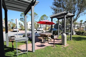 Un espacio al aire libre con patio, una mesa de madera y bancos, una sombrilla roja y un cubo de basura.