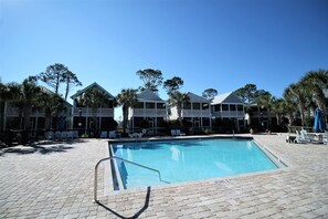 A swimming pool with a brick deck, surrounded by lounge chairs and umbrellas, with beachfront houses in the background. - SEAS THE DAY IS A PRIVATE 2BD COTTAGE WITH 3 COMMUNITY POOLS, PET FRIENDLY! (Port Saint Joe)