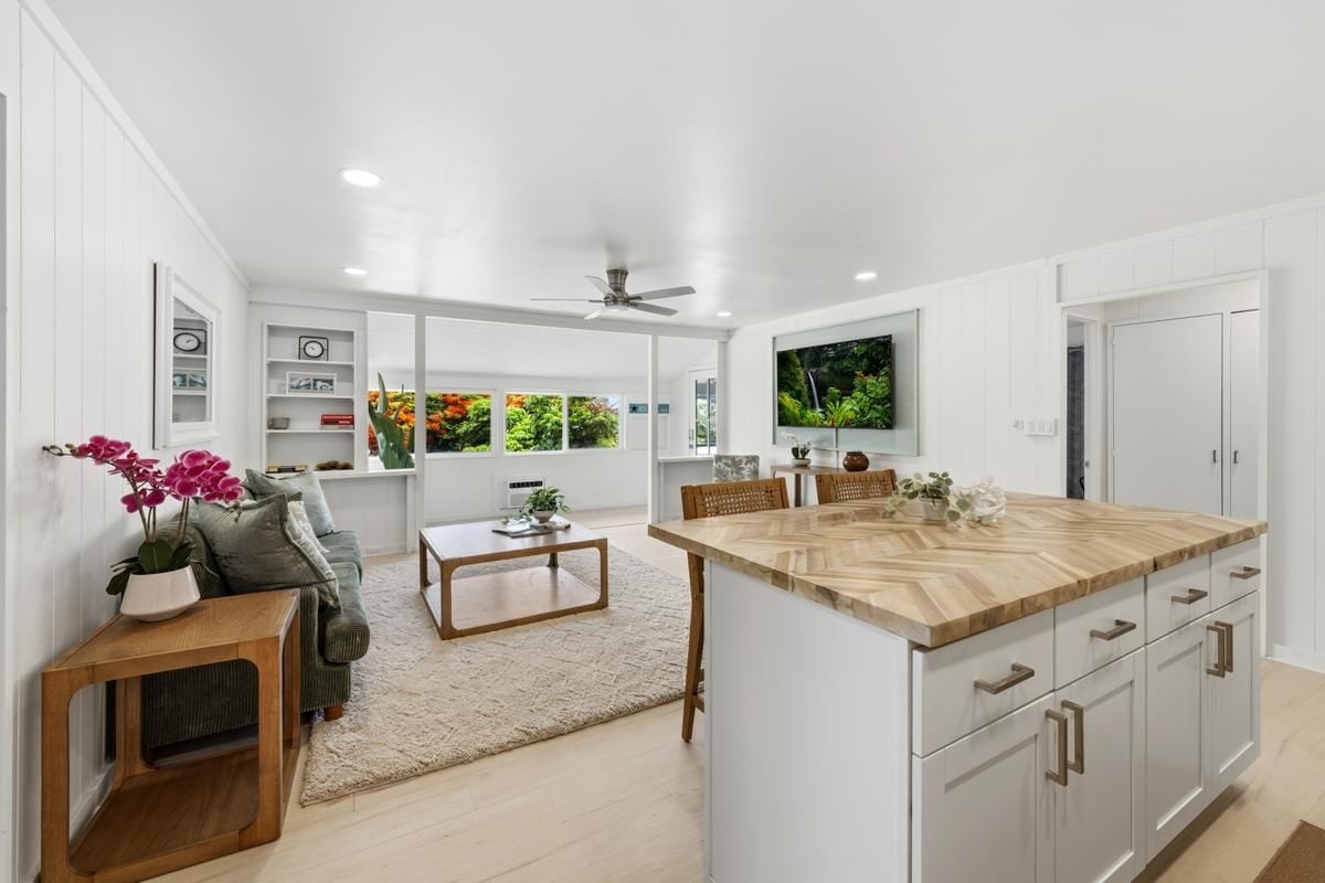 A modern kitchen with white cabinetry, a wooden island, and a dining area with a sofa and coffee table.