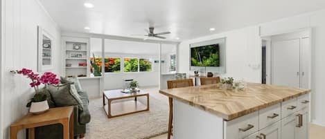 A modern kitchen with white cabinetry, a wooden island, and a dining area with a sofa and coffee table.