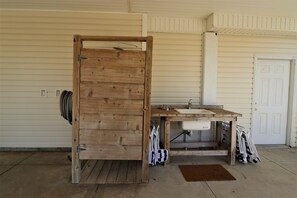 Uma porta de madeira rústica dá acesso a um banheiro com pia e chuveiro.