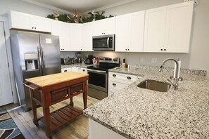 Une cuisine avec des meubles blancs, des appareils en acier inoxydable, un comptoir en granit et une table en bois.