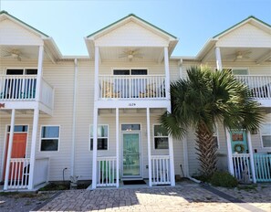 A row of three-story buildings with balconies, a green door, and a palm tree. - PELICAN PERCH IS A 3BD/2BA  TOWNHOUSE JUST STEPS TO BEACH AND SHOPS! (Mexico Beach)