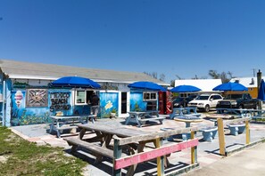 Un espace extérieur aménagé sur le thème de la plage, avec des tables et des parasols, une fresque murale et un camion-restaurant.