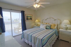 A bedroom with a bed, two bedside tables, a ceiling fan, a window with curtains, and a painting on the wall. - PELICAN PERCH IS A 3BD/2BA  TOWNHOUSE JUST STEPS TO BEACH AND SHOPS! (Mexico Beach)