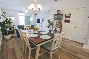 A dining area with a wooden table, four chairs, a chandelier, and a potted plant. - PELICAN PERCH IS A 3BD/2BA  TOWNHOUSE JUST STEPS TO BEACH AND SHOPS! (Mexico Beach)