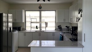 Una cucina moderna con mobili bianchi, un frigorifero in acciaio inossidabile, un lavello doppio e una finestra con persiane.