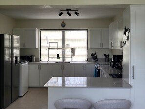 A modern kitchen with white cabinets, a stainless steel refrigerator, a double sink, and a window with blinds. - Modern 2 bed 2 bath home away from home perfectly located for visitors (Bridgetown)