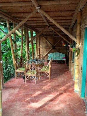 A covered outdoor area with bamboo structures, a table with chairs, and a hammock. - Jui Chi MaMa Ecolodge & Birding (PALOMINO)