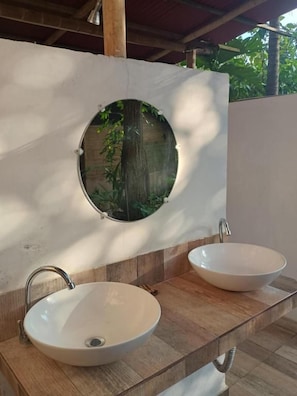 A bathroom with a wooden vanity, two white sinks, and a circular window with a view of greenery. - Jui Chi MaMa Ecolodge & Birding (PALOMINO)
