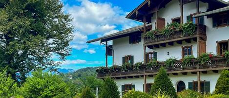 A multi-story building with balconies, surrounded by lush greenery and a clear sky.
