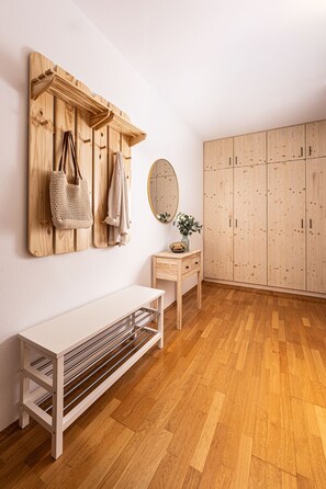 Une pièce avec un plancher en bois, un banc, un miroir, une petite table et une armoire.