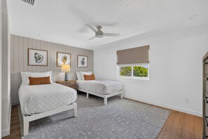 A bedroom with two beds, a ceiling fan, a window with a view, and framed artwork on the wall. - Riverfront Retreat | Dock & River Access | Kayak (St. Augustine)