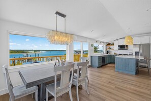 A modern kitchen with a view of the sea, wooden flooring, and a dining area with a table and chairs. - Riverfront Retreat | Dock & River Access | Kayak (St. Augustine)