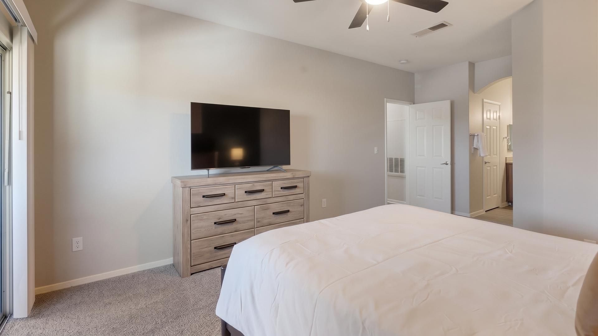 A bedroom with a bed, a dresser, a television, and a door leading to another room.