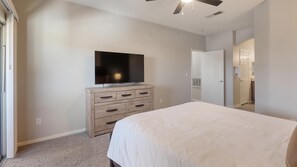 A bedroom with a bed, a dresser, a television, and a door leading to another room.