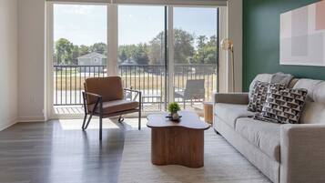 A living room with a sofa, armchair, coffee table, and a view through a glass door to an outdoor patio.