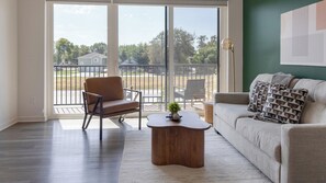 A living room with a sofa, armchair, coffee table, and a view through a glass door to an outdoor patio.