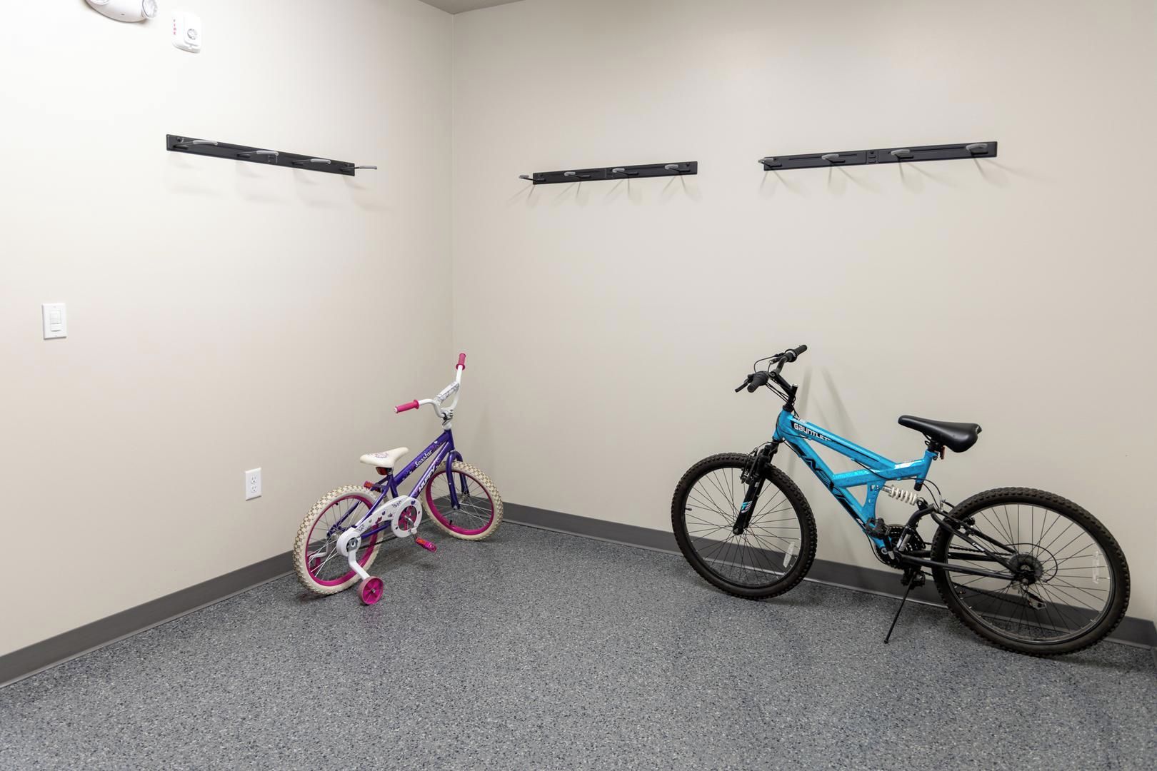 A room with two bicycles, a wall-mounted shelf, and a power outlet.