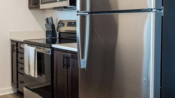 A modern kitchen with stainless steel appliances, dark wooden cabinets, and a light wood floor.