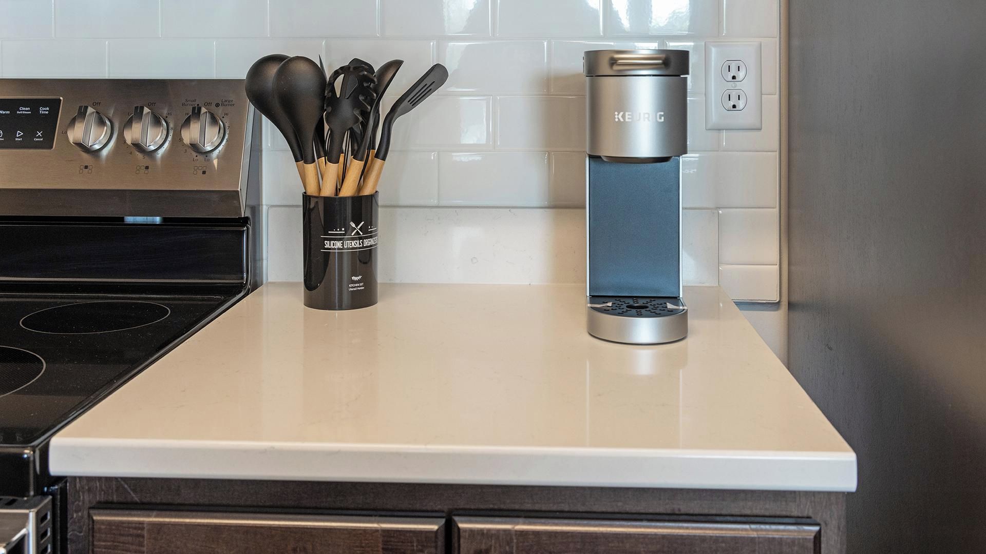 A kitchen counter with a coffee maker, a set of utensils, and a stove.