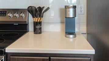 A kitchen counter with a coffee maker, a set of utensils, and a stove.