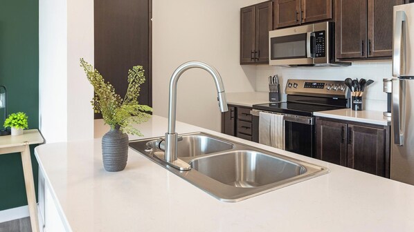 A modern kitchen with stainless steel appliances, a double sink, and dark wooden cabinets.