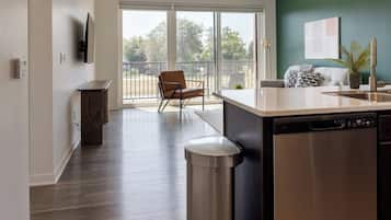 A modern kitchen with a dishwasher, a dining area with a chair, and a view through a glass door to an outdoor balcony.