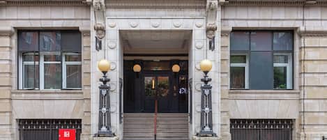 A building entrance with a grand archway, steps leading up to a door, and two street lamps on either side.