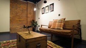 Ein Zimmer mit einer Ziegelwand, einer Holzkiste, einem braunen Ledersofa und einem Blumentopf.