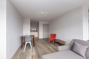 Ein modernes Wohnzimmer mit einem grauen Sofa, einem roten Sessel und einem Essbereich mit Tisch und Stühlen.