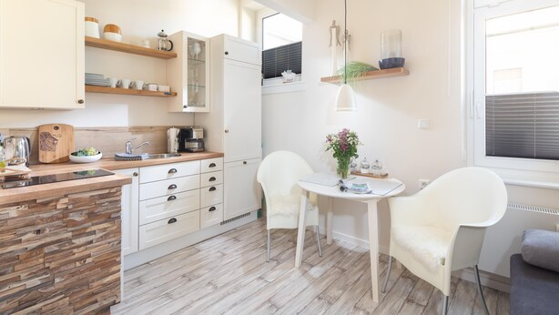 A modern kitchen with wooden cabinets, a dining table with chairs, and a small island with a kettle. - Vrbo Property (Norderney)