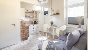A modern living room with a grey sofa, a small round table, and a kitchen area with white cabinets and a wooden countertop. - Vrbo Property (Norderney)