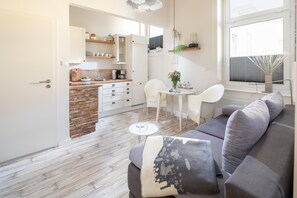 Ein modernes Wohnzimmer mit einem grauen Sofa, einem kleinen runden Tisch und einer Küchenzeile mit weißen Schränken und einer Holz Arbeitsplatte.